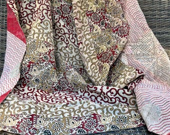 May include: A cream and red patterned quilt with a floral design. The quilt is folded and draped over a wicker chair.