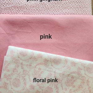 May include: Three different pink fabrics are displayed. The top fabric is pink gingham. The middle fabric is a solid pink. The bottom fabric is floral pink with a white background and pink floral pattern.