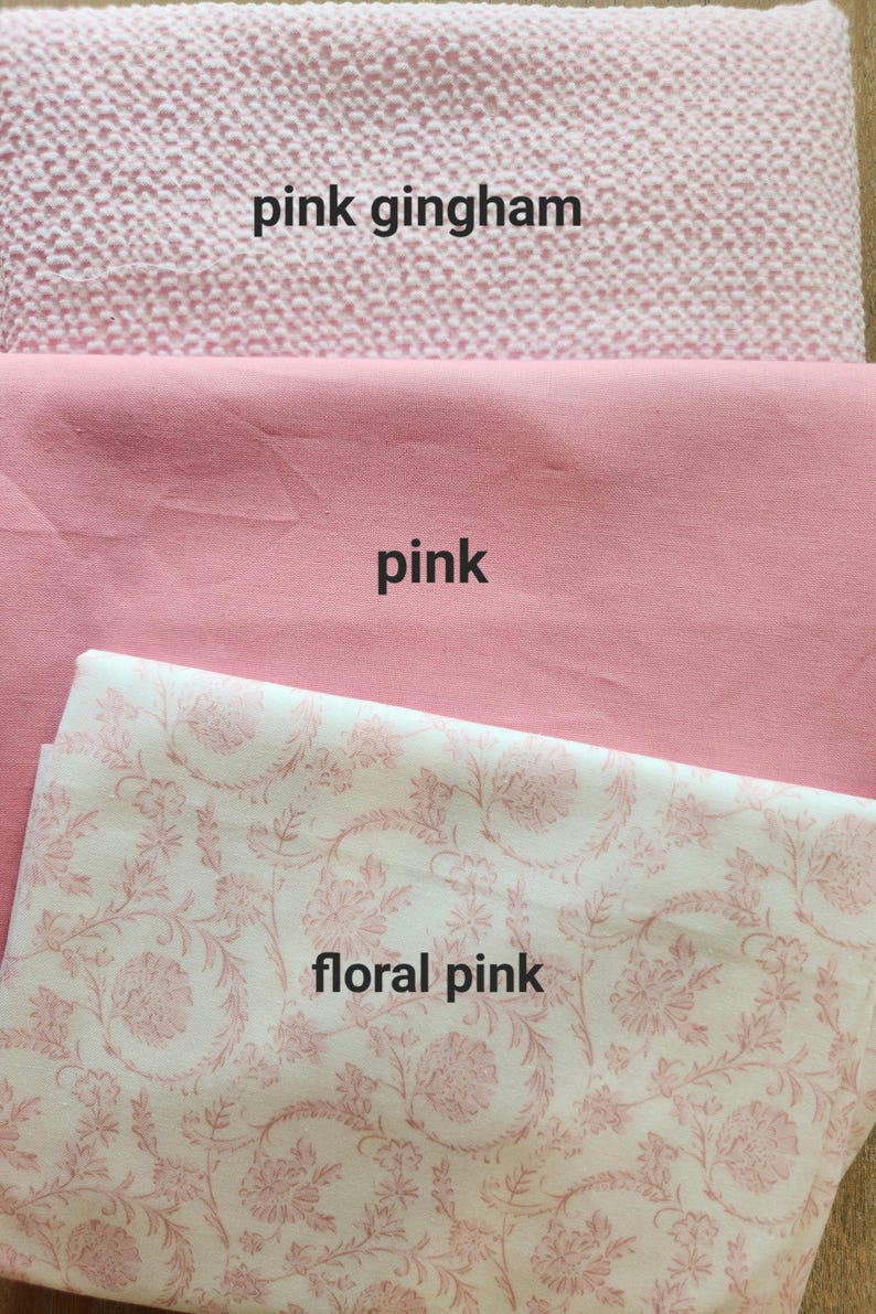 May include: Three different pink fabrics are displayed. The top fabric is pink gingham. The middle fabric is a solid pink. The bottom fabric is floral pink with a white background and pink floral pattern.