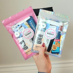May include: Two clear plastic bags filled with various small items, including wipes, lip balm, and electrolyte mix. One bag is pink, the other is iridescent. Each bag has a sticker that says "Last Rodeo Hangover Kit" and "Wipe That Tush."
