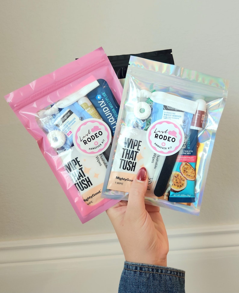 May include: Two clear plastic bags filled with various small items, including wipes, lip balm, and electrolyte mix. One bag is pink, the other is iridescent. Each bag has a sticker that says "Last Rodeo Hangover Kit" and "Wipe That Tush."