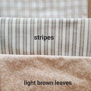 May include: Close-up of three fabric swatches. The top swatch is neutral gingham, the middle swatch has stripes, and the bottom swatch features light brown leaves. The text "neutral gingham", "stripes", and "light brown leaves" are printed on the fabric.