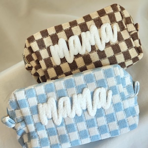May include: Two rectangular cosmetic bags. One is brown and beige checkered, the other is blue and white checkered. Both bags have the word "mama" in white, fluffy letters across the front.