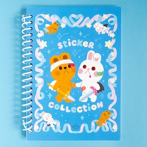 May include: A blue spiral bound notebook with a sticker collection theme. The cover features a cartoon illustration of two animal characters, a bear and a rabbit, with the words "sticker collection" in the centre.