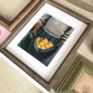 May include: A framed painting of a person holding a basket of lemons. The person is wearing a blue and white striped shirt and a blue skirt. The lemons are yellow and are arranged in a basket.