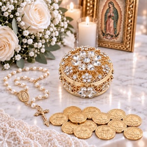 May include: A round gold-tone metal trinket box featuring intricate filigree patterns and clear crystal floral accents on the lid and sides. The box is accompanied by a white pearl rosary with a gold-tone crucifix and several gold-colored coins.