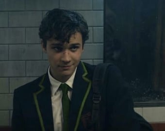 May include: A person wearing a dark navy blazer with green trim and a green tie, paired with a white collared shirt. The blazer has a crest on the chest. A black backpack is visible.