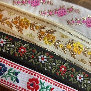 May include: Close-up of several decorative ribbons with floral patterns. The ribbons feature various colours, including white, black, and red, with embroidered flowers and gold accents. The ribbons are ideal for crafting and embellishments.