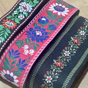 Könnte beinhalten: Nahaufnahme von drei dekorativen Bändern mit floralen Mustern. Die Bänder haben schwarze, rote und marineblaue Hintergründe mit weißen, blauen und roten Blumendesigns. Die Bänder sind aufgerollt und zeigen die detaillierte Stickerei.