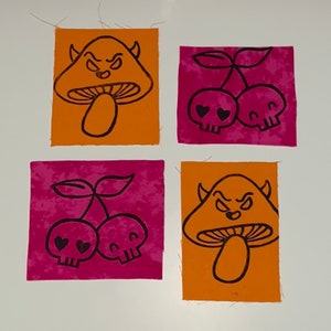 May include: Four fabric squares with black line art. Two squares feature an orange mushroom with a devilish face. The other two squares have pink backgrounds with cherries and skull faces.