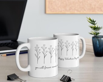 May include: Two white ceramic mugs with black line art of floral stems with heart-shaped flowers. One mug reads "you will forever remain in" and the other says "Happy Valentines Day 2020".