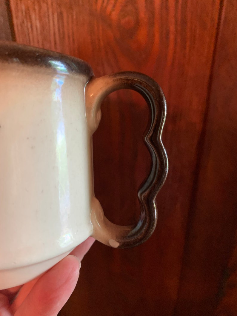 May include: A white ceramic pitcher with a brown handle. The handle has a scalloped edge.