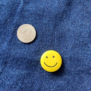 May include: A silver US quarter coin and a yellow smiley face button on a blue denim background.