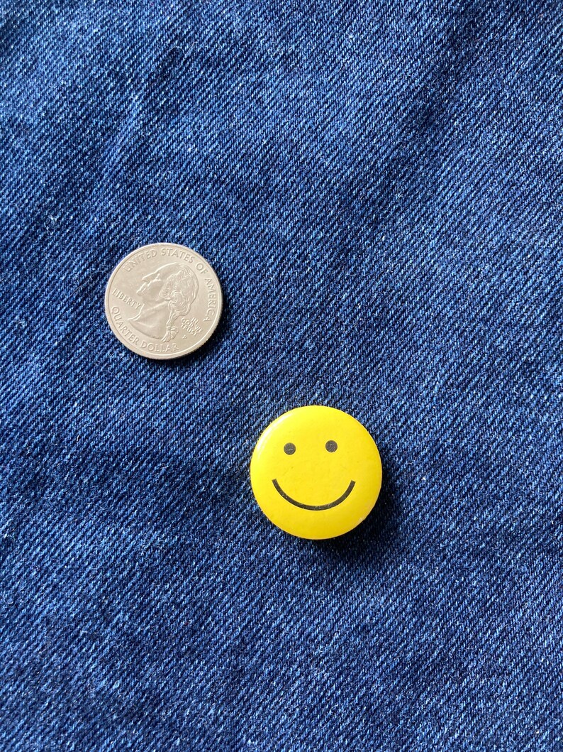 May include: A silver US quarter coin and a yellow smiley face button on a blue denim background.