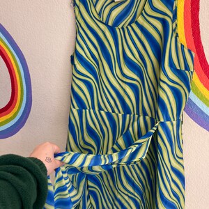 May include: A sleeveless dress with a blue and green wavy pattern. The dress has a scoop neck and a tie at the waist.