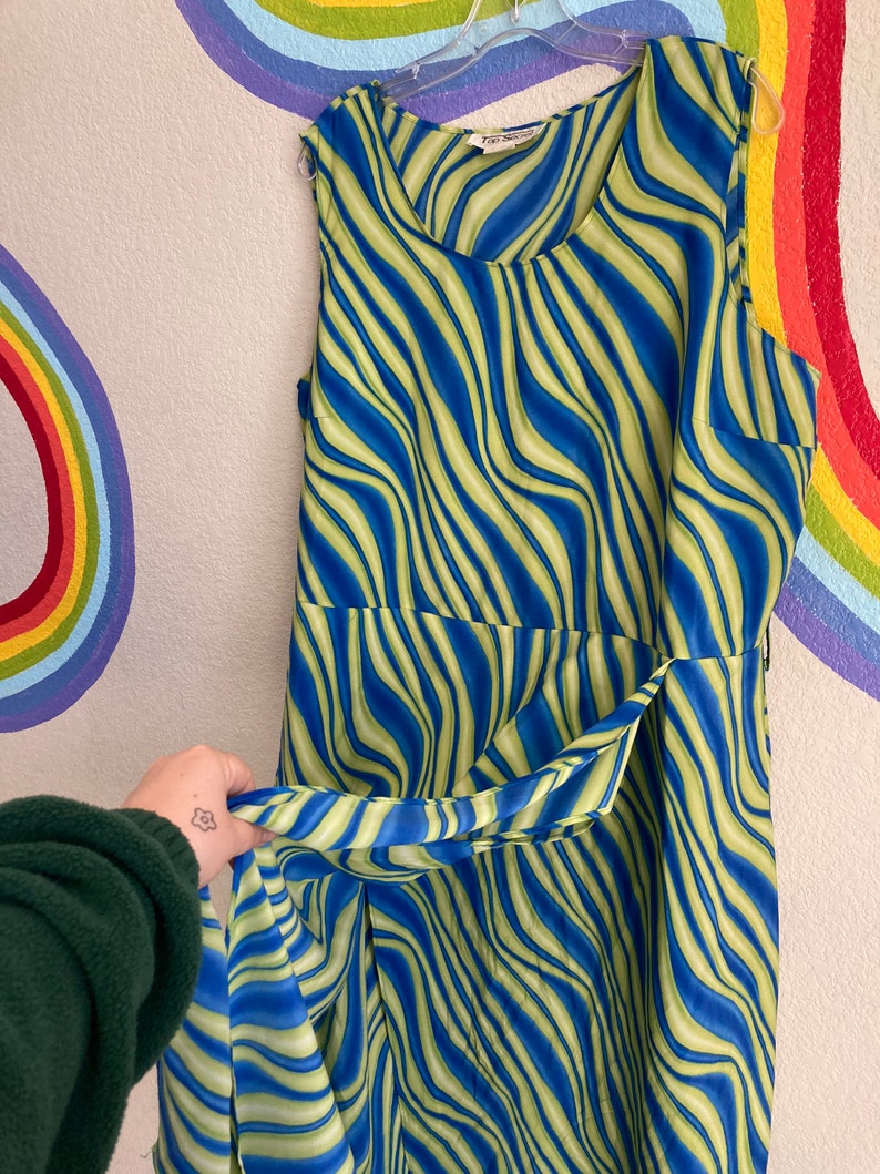 May include: A sleeveless dress with a blue and green wavy pattern. The dress has a scoop neck and a tie at the waist.