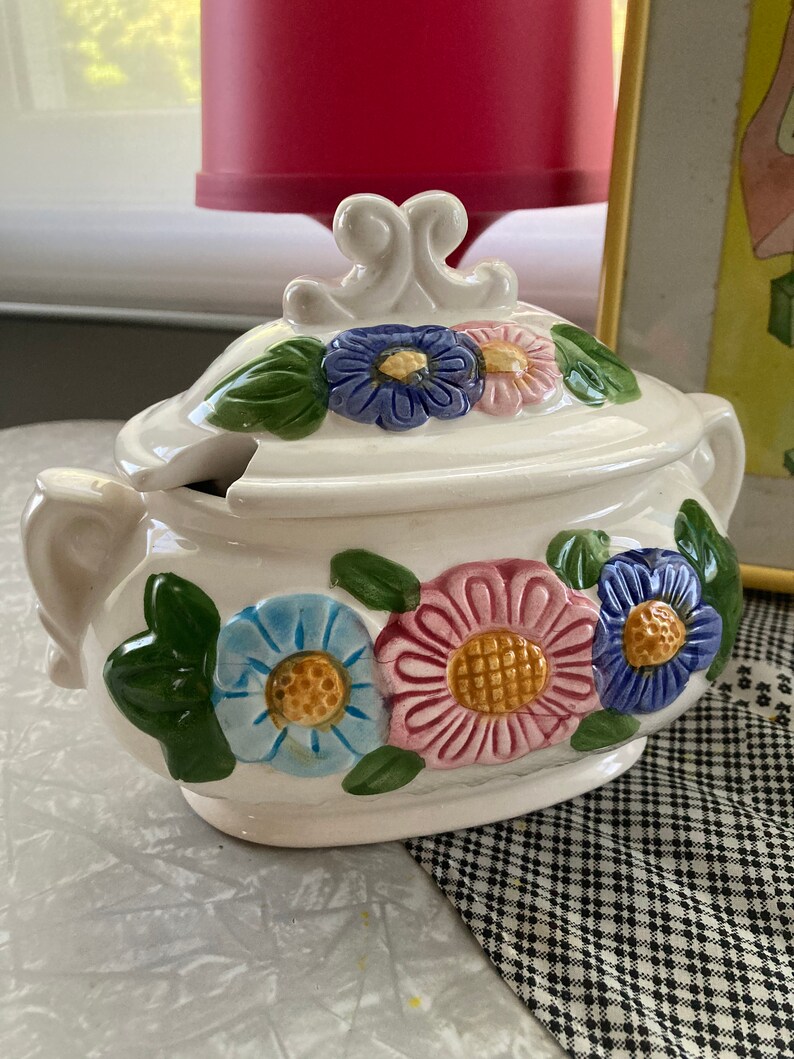 May include: White ceramic serving dish with a lid. The lid has a floral design with blue, pink, yellow, and green flowers. The dish has a similar floral design with blue, pink, and yellow flowers.