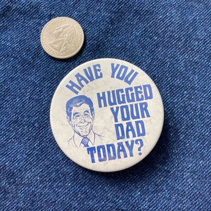 May include: A white button with blue text that reads "Have you hugged your dad today?"  A cartoon image of a man with brown hair and a blue tie is in the center of the button.