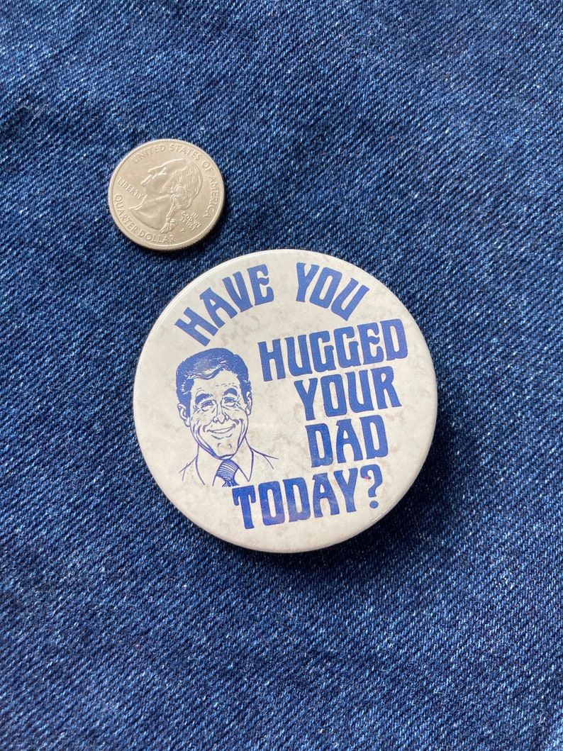 May include: A white button with blue text that reads "Have you hugged your dad today?"  A cartoon image of a man with brown hair and a blue tie is in the center of the button.