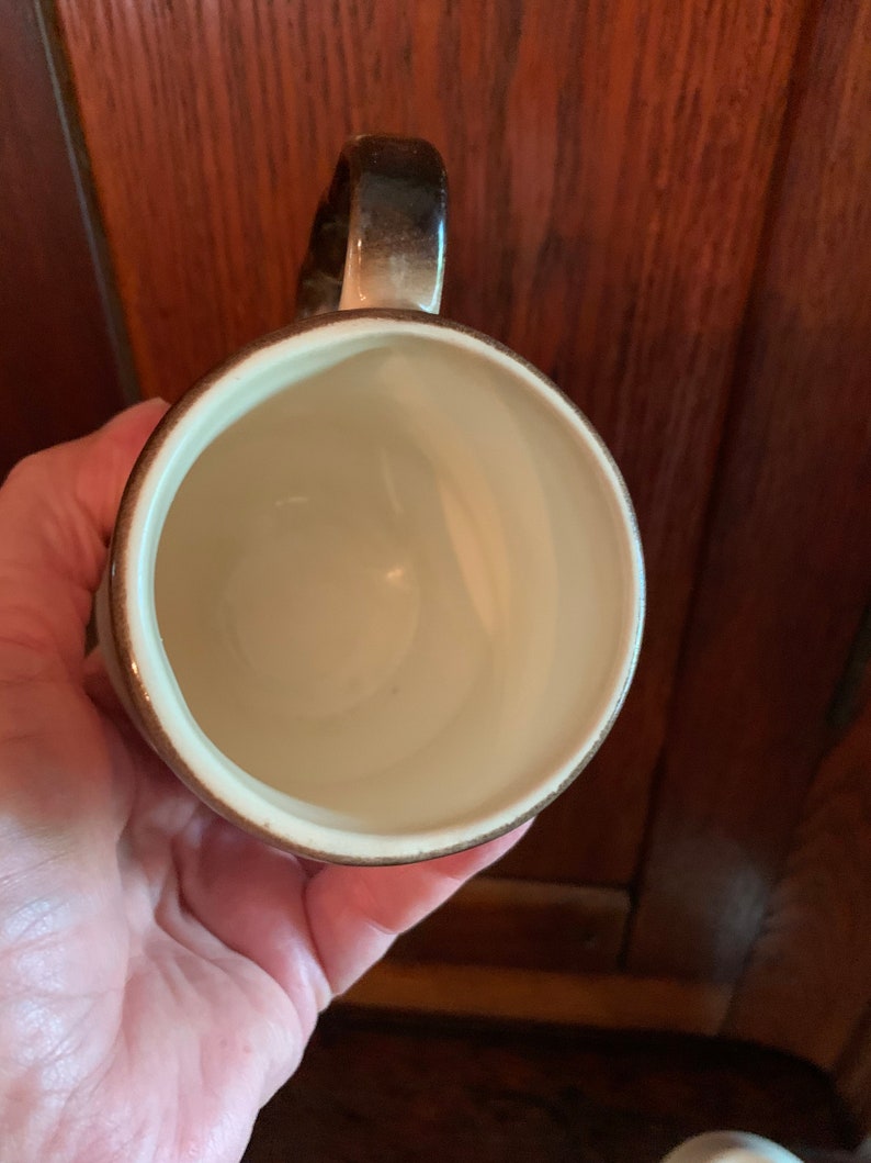May include: A brown and white ceramic mug with a rounded handle. The mug is empty and has a white interior.