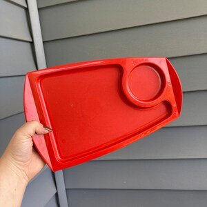 May include: A bright red plastic tray with a small circular indentation. The tray is designed for serving food or drinks.