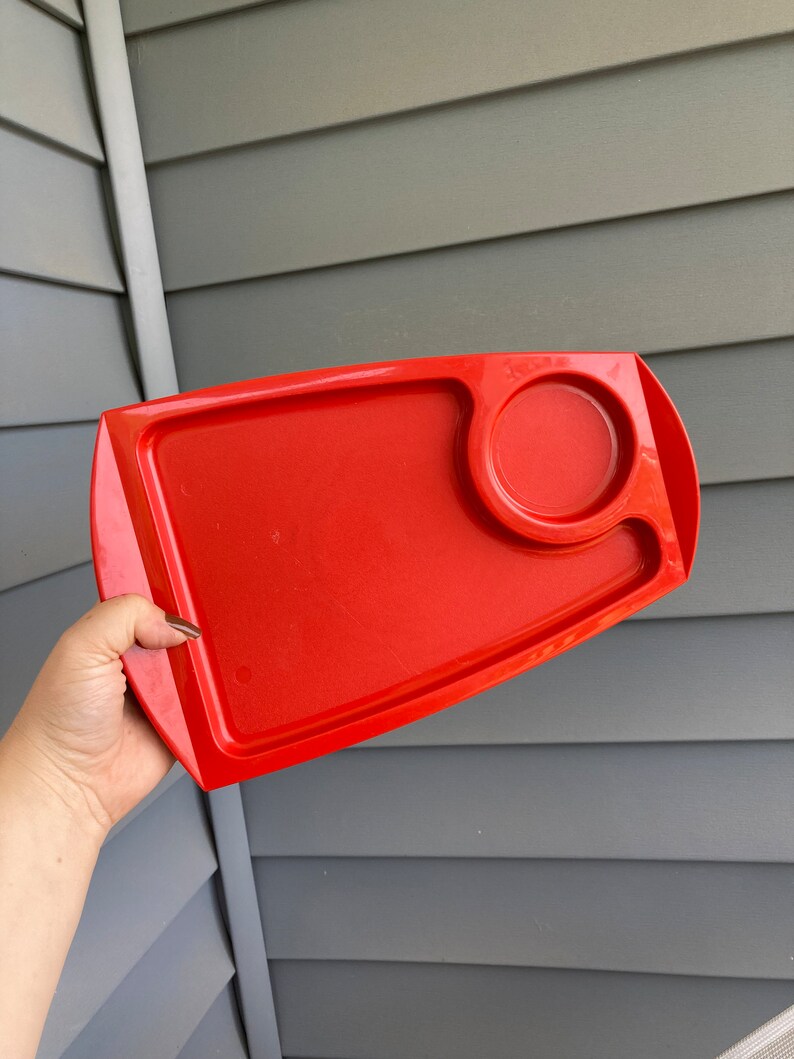 May include: A bright red plastic tray with a small circular indentation. The tray is designed for serving food or drinks.