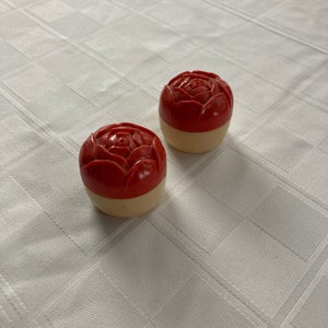May include: Two small, round, red and white containers with a rose design on the top. The containers are made of plastic and have a vintage look.
