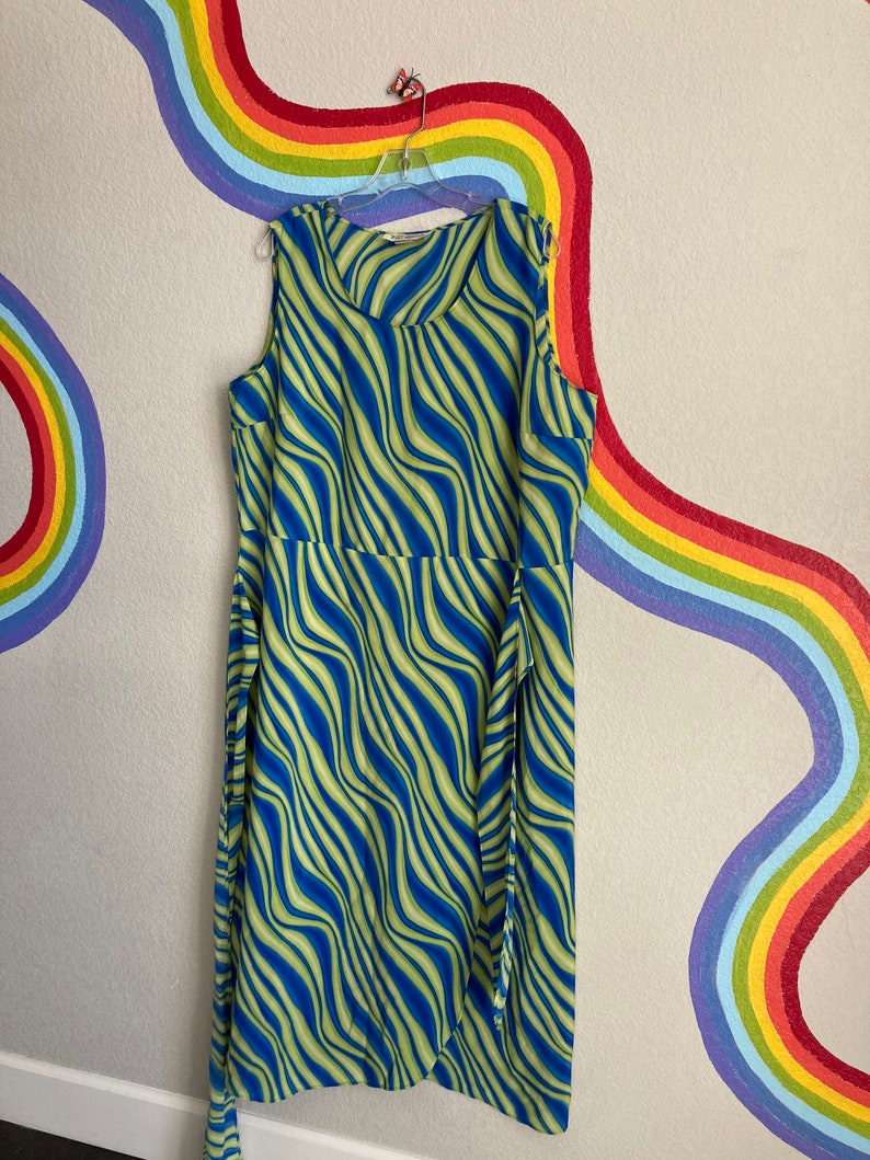 May include: A sleeveless maxi dress with a blue and green wavy pattern. The dress has a scoop neck and a tie at the waist.