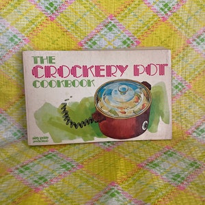 May include: A vintage cookbook titled "The Crockery Pot Cookbook" with a red crockpot on the cover. The crockpot has a glass lid and is filled with food. The cookbook has a yellow background with green and pink plaid.