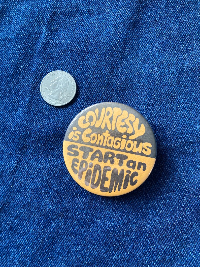 May include: A round button with a black and gold design. The text on the button reads "Courtesy is contagious. Start an epidemic."