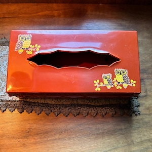 May include: A rectangular orange tissue box cover featuring a glossy finish and decorative illustrations of three owls perched on branches. The owls are rendered in shades of yellow and brown, positioned on the top surface of the container.