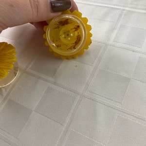 May include: Two yellow plastic salt and pepper shakers shaped like sunflowers. The shakers have a clear plastic top with holes for dispensing salt and pepper.