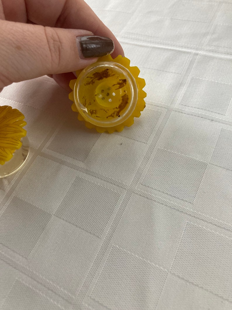 May include: Two yellow plastic salt and pepper shakers shaped like sunflowers. The shakers have a clear plastic top with holes for dispensing salt and pepper.