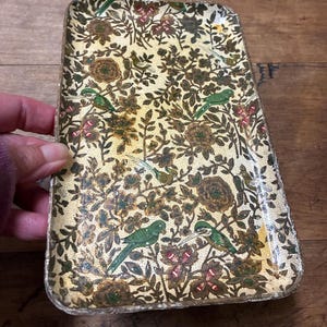 May include: A rectangular tray featuring a cream-colored background with a dense, repeating pattern of green birds, brown flowers, and dark green foliage. The tray has slightly raised edges and a worn, textured finish along the outer perimeter.