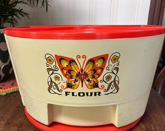May include: Cream-coloured flour container with a bright orange rim and base. A colourful butterfly graphic is centered on the front, with the word "FLOUR" below. The container is made of plastic and has a retro design.
