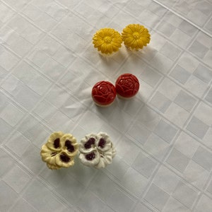 May include: Five ceramic flower-shaped knobs in yellow, red, and white. The knobs have a raised design and are perfect for adding a touch of whimsy to furniture.