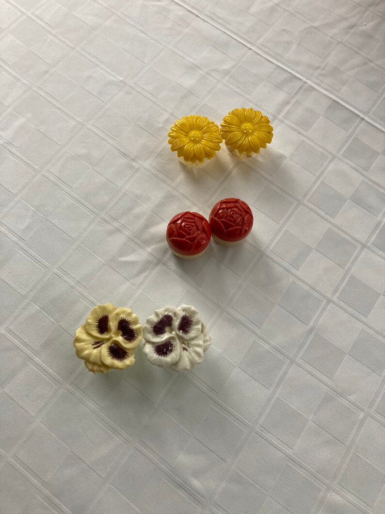 May include: Five ceramic flower-shaped knobs in yellow, red, and white. The knobs have a raised design and are perfect for adding a touch of whimsy to furniture.