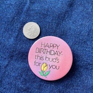 May include: A pink button with the text "Happy Birthday- this bud's for you" and a yellow flower illustration.