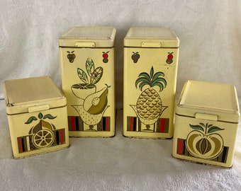 May include: Set of four vintage yellow metal canisters with fruit designs. The canisters have a white lid and feature a pineapple, a pear, a lemon, and an apple.