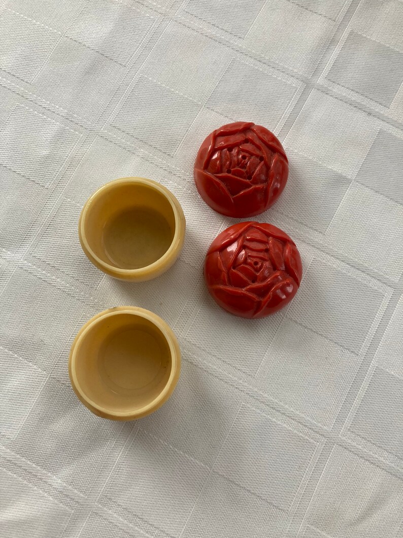 May include: Two small, round, red boxes with a rose design on the top and two small, round, cream-colored boxes.