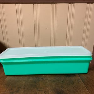 May include: A rectangular storage container with a bright green base and a flat, opaque white lid. The container features a long, narrow shape with straight sides and a smooth finish, designed for food storage or organization in a kitchen setting.