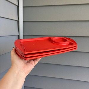 May include: Three red plastic trays with a small indented circle on the top tray. The trays are stacked on top of each other.