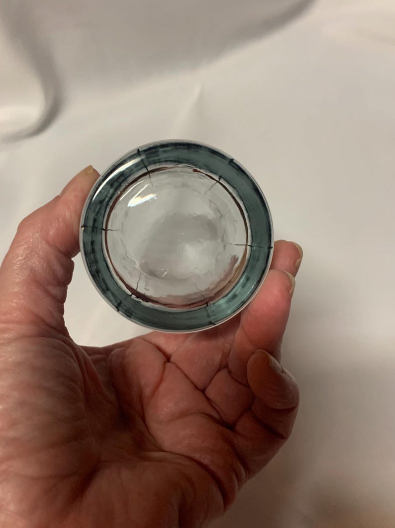 Puede incluir: Un vaso de chupito de vidrio transparente con un borde azul y rojo. El vaso tiene una superficie texturizada.