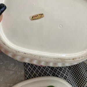 May include: White ceramic lidded dish with a floral design. The lid has a gold sticker that reads "Shiah Yihi Made in Taiwan."