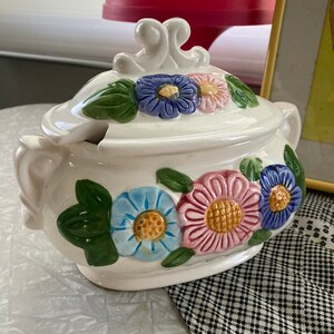 May include: White ceramic serving dish with a lid. The dish is decorated with colorful flowers and green leaves. The lid has a decorative handle.
