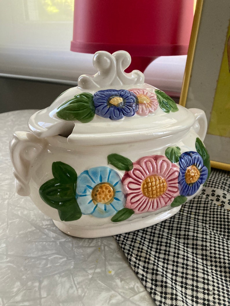 May include: White ceramic serving dish with a lid. The dish is decorated with colorful flowers and green leaves. The lid has a decorative handle.