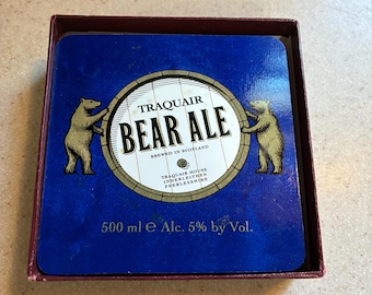 May include: A set of square beer coasters in a box. Each coaster features a blue background with the text "TRAQUAIR BEAR ALE" in a circular design, with two bear illustrations. The text "500 ml e Alc. 5% by Vol." is also visible.