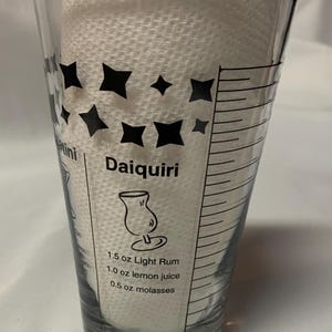 Puede incluir: Un vaso medidor de vidrio transparente con marcas negras y una receta para un Daiquiri. La receta incluye 1,5 oz de ron blanco, 1,0 oz de jugo de lim&oacute;n y 0,5 oz de melaza.