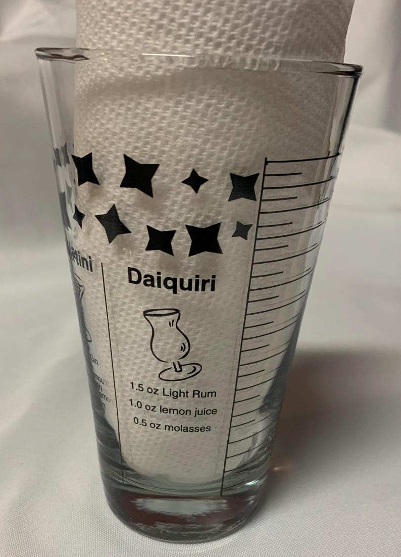 Puede incluir: Un vaso medidor de vidrio transparente con marcas negras y una receta para un Daiquiri. La receta incluye 1,5 oz de ron blanco, 1,0 oz de jugo de lim&oacute;n y 0,5 oz de melaza.