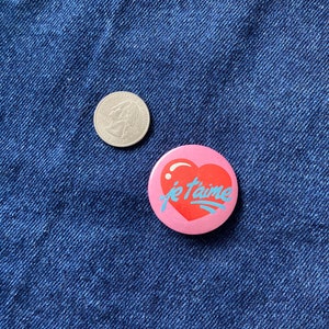 May include: A pink heart-shaped button with the text "je t'aime" in blue lettering.